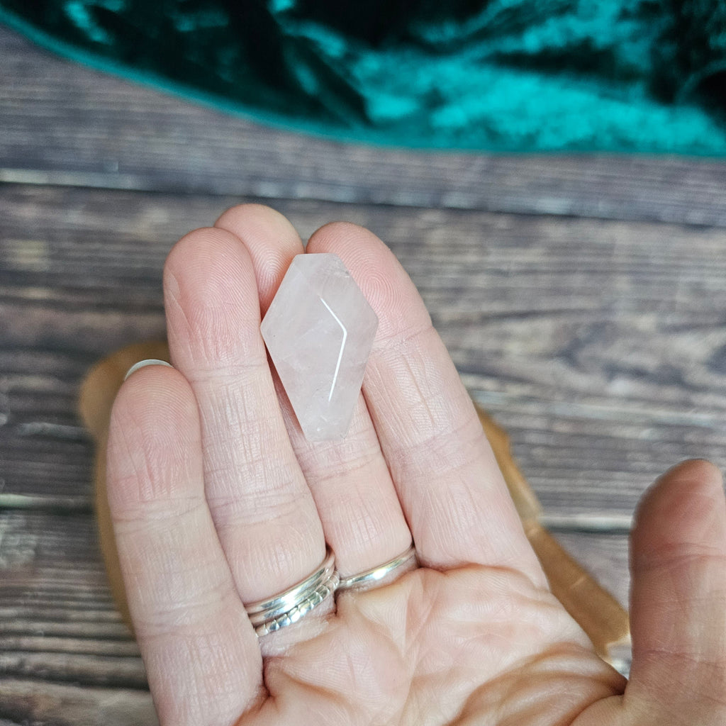 A pink crystal shaped as a coffin is being held in someone's hand