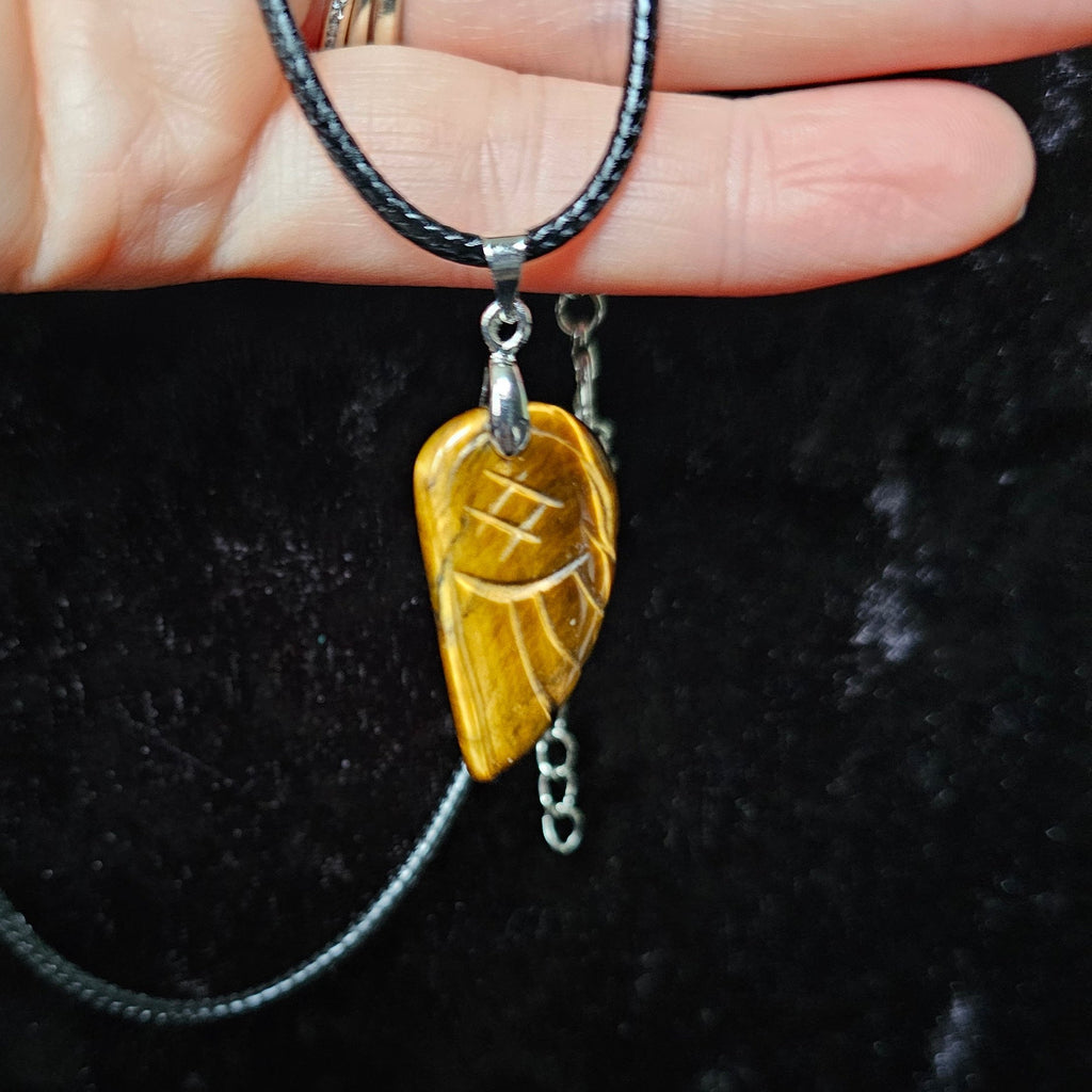 An angel wing-shaped crystal pendant attached to a black cord necklace, held in a person's hand.
