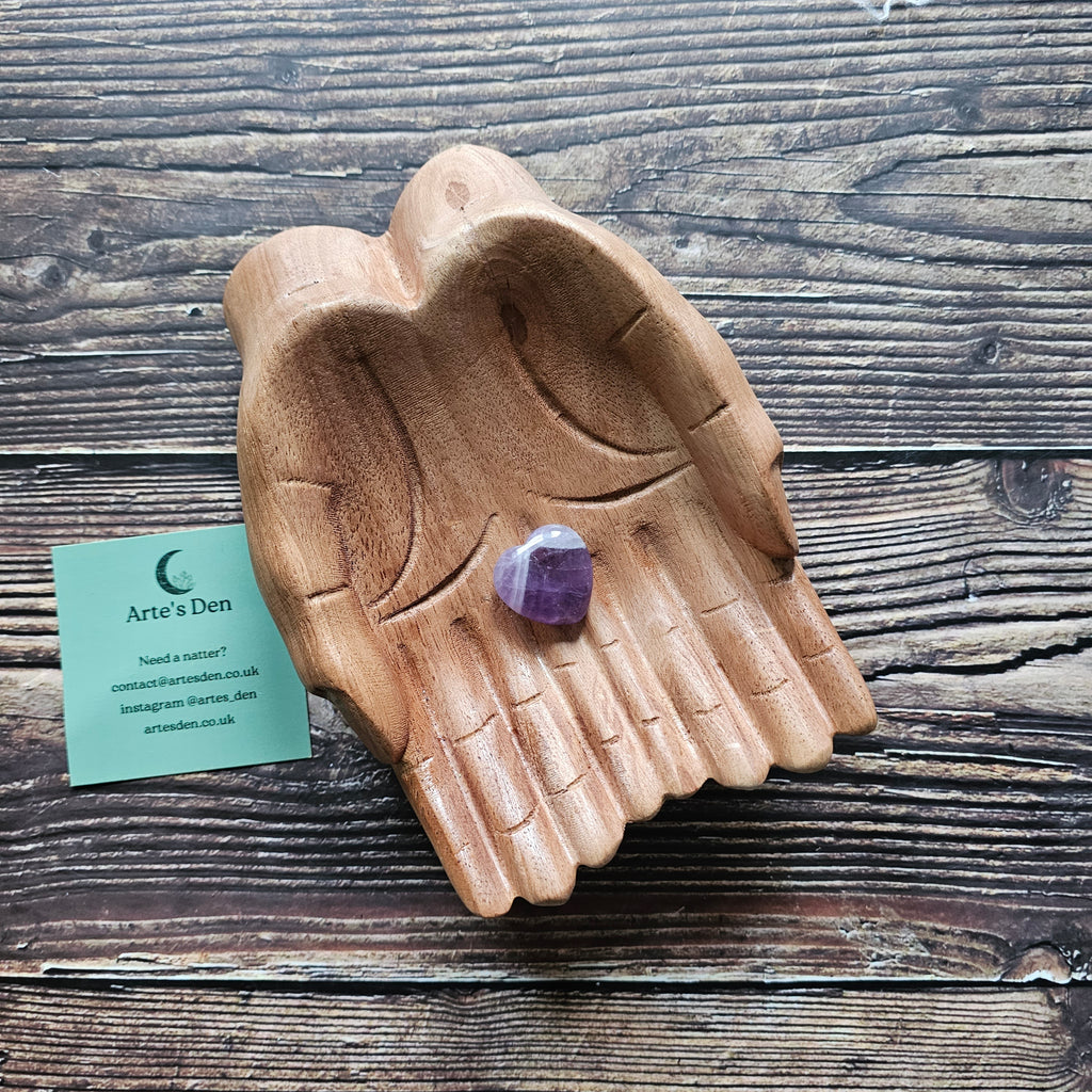 An amethyst crystal heart on a pair of wooden hands. 