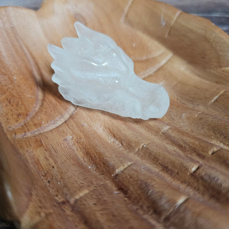 A clear quartz crystal dragon skull figurine, placed on a wooden surface.