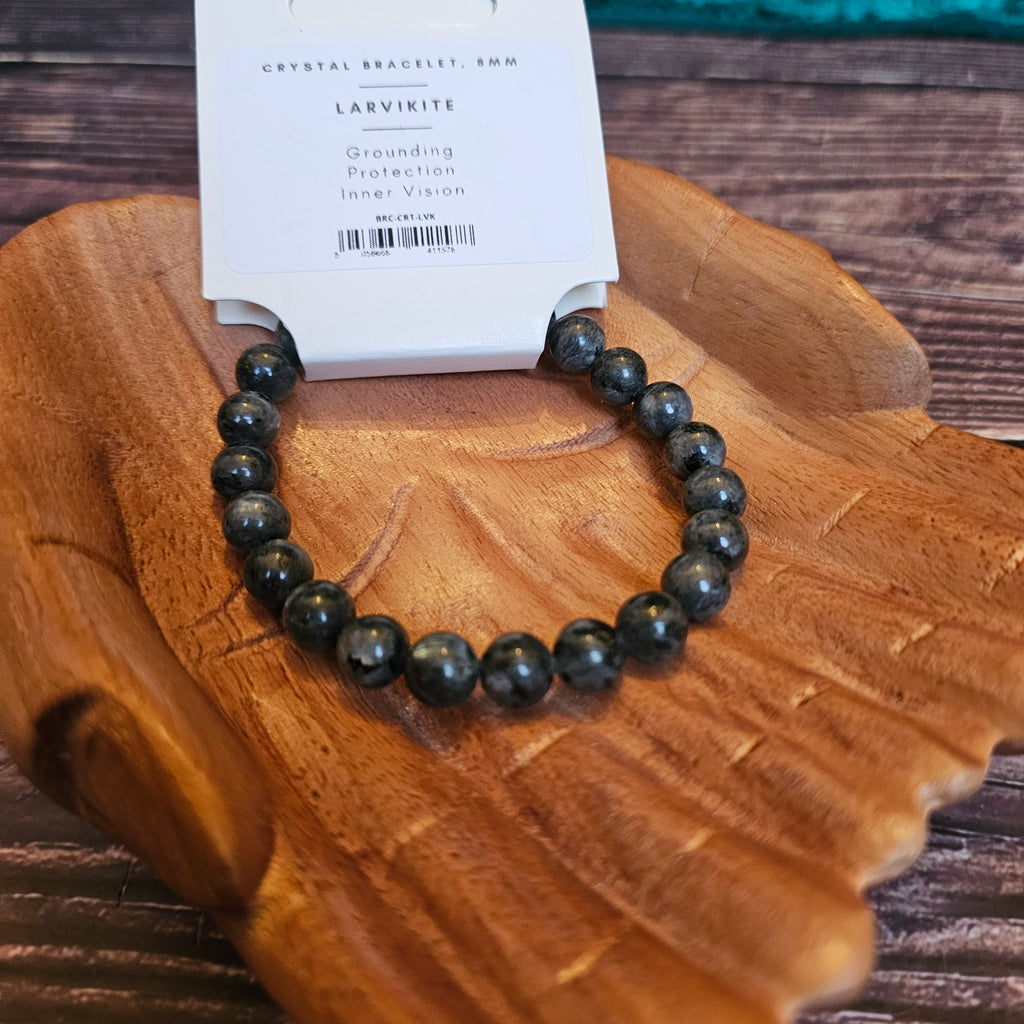A beaded bracelet with black and gray stones, displayed on a wooden bracelet holder with a card in the background indicating the product is called 'Larvikite Beaded Bracelet' 