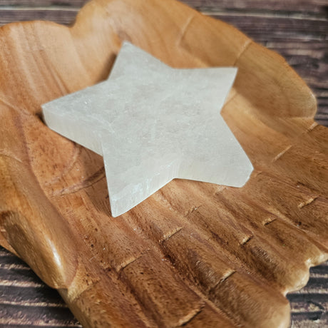 A selenite crystal charging plate shaped as a star, placed on a wooden pair of hands