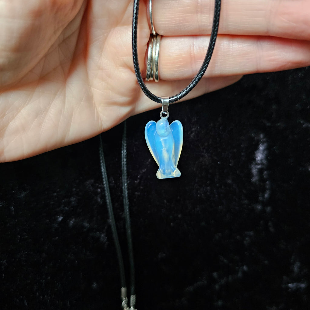 An angel-shaped crystal pendant attached to black cord necklace held in a person's hand on a dark background