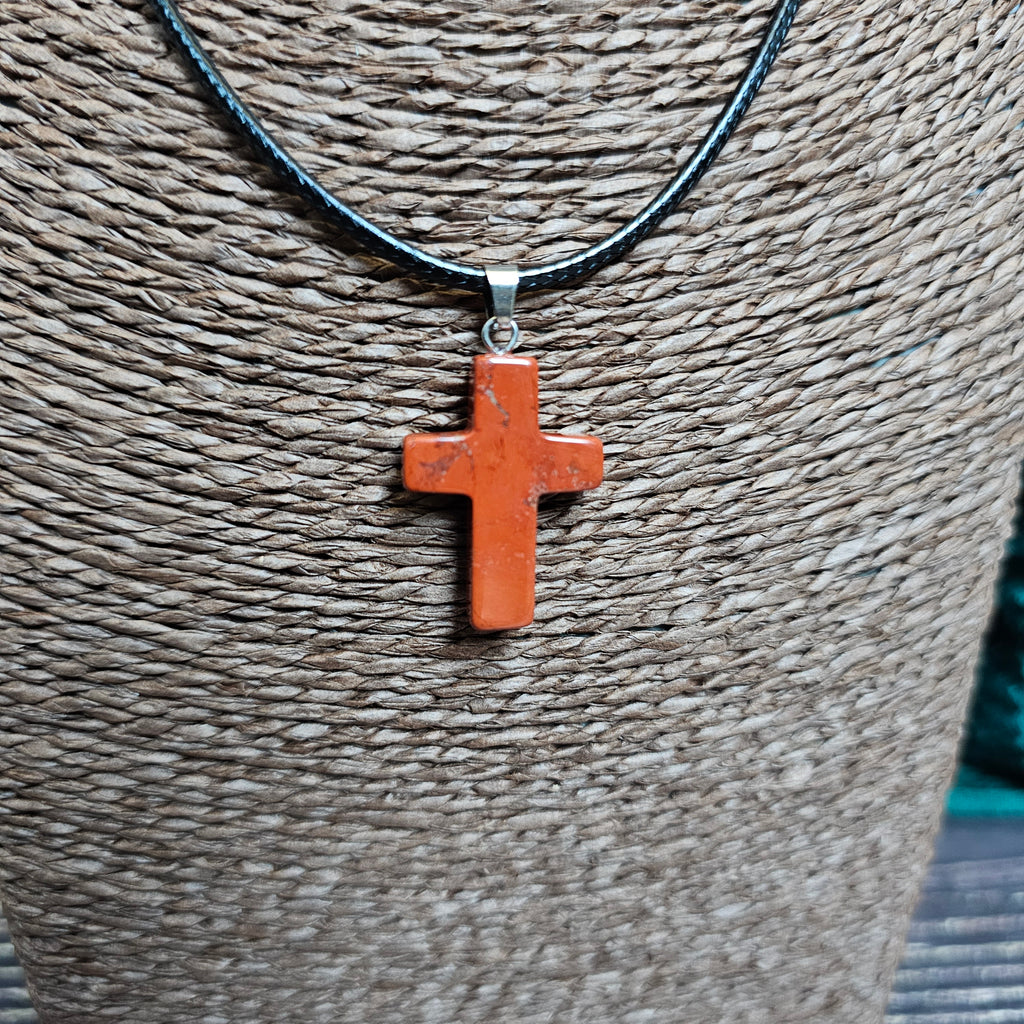 A cross-shaped crystal pendant with a black cord necklace displayed on a textured background.