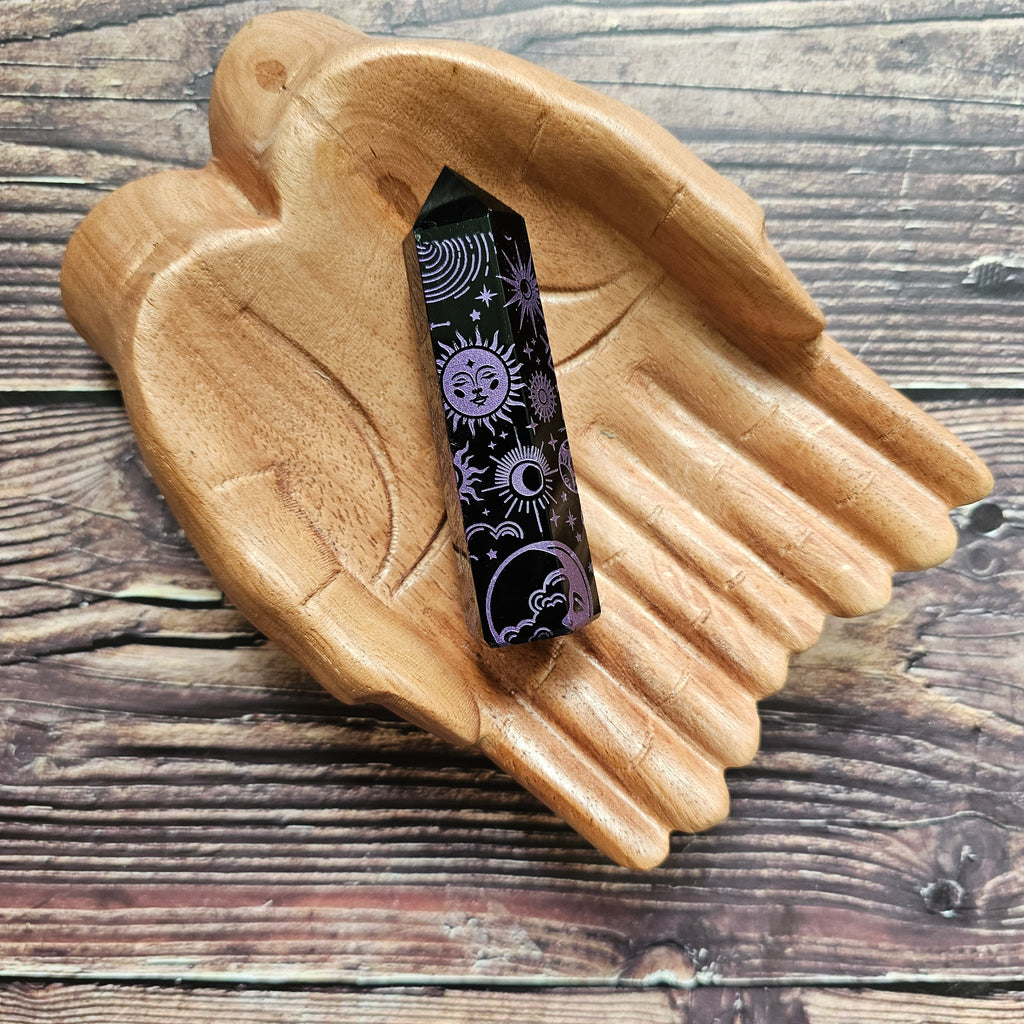 A Black Obsidian Generator with celestial designs displayed on a wooden hand-shaped tray.