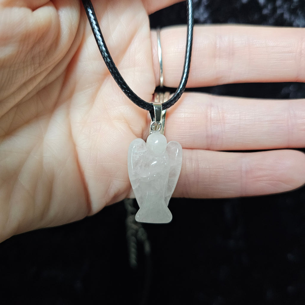 An angel-shaped crystal pendant attached to black cord necklace on a dark background