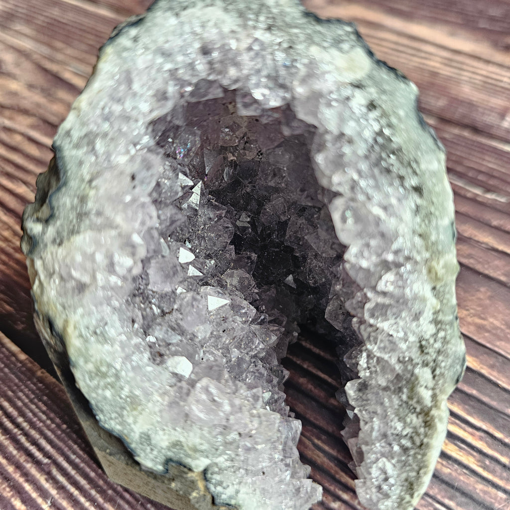 A rough, opaque purple Amethyst crystal in a standing cluster shape on a wooden surface.