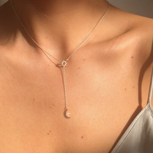 A person wears a silver lariat necklace featuring a crescent moon and an open sun charm.