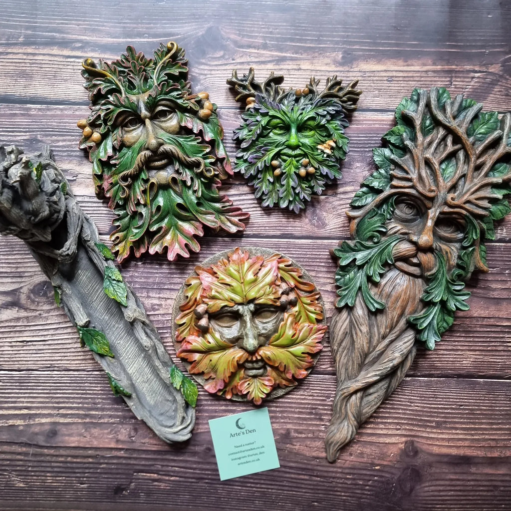 A collection of different plaques in the green man design as well as an incense holder, all against a wooden background