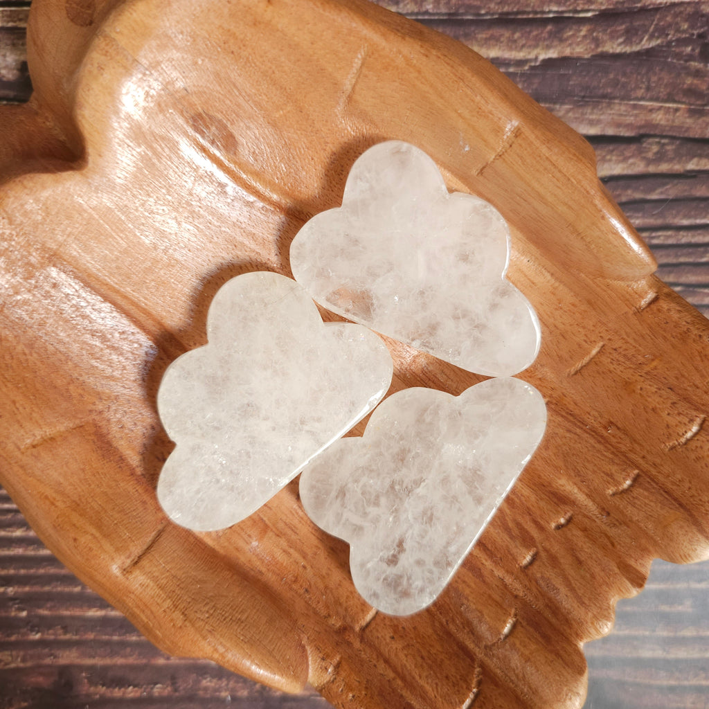 Carved clear quartz crystals shaped like clouds, placed on a wooden surface.