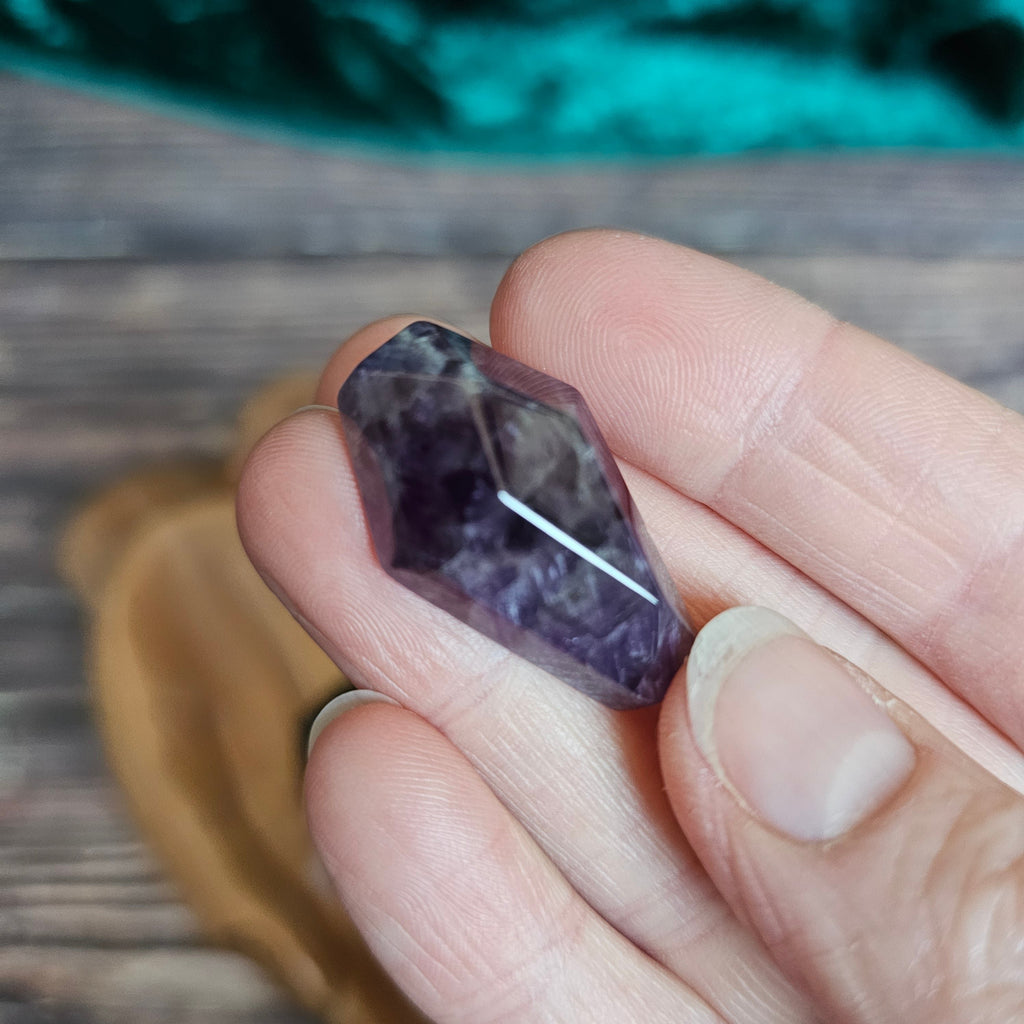 An Amethyst crystal coffin is being held in someone's hand
