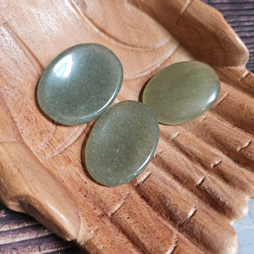 Three green polished crystal thumbstones resting on a wooden surface