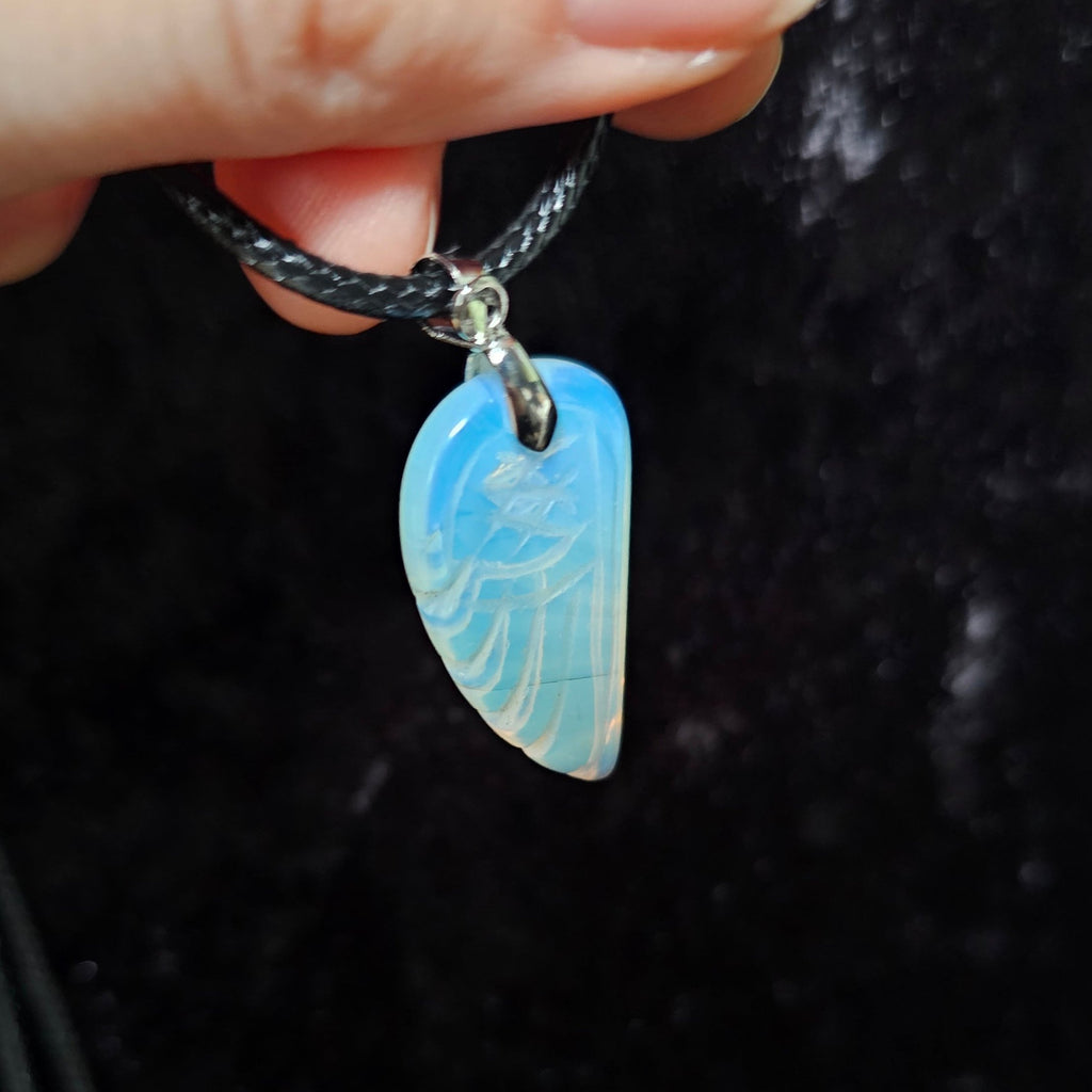 An angel wing-shaped crystal pendant attached to a black cord necklace, held in a person's hand.