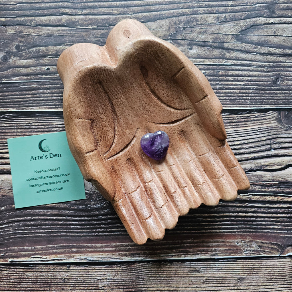An amethyst crystal heart on a pair of wooden hands. 