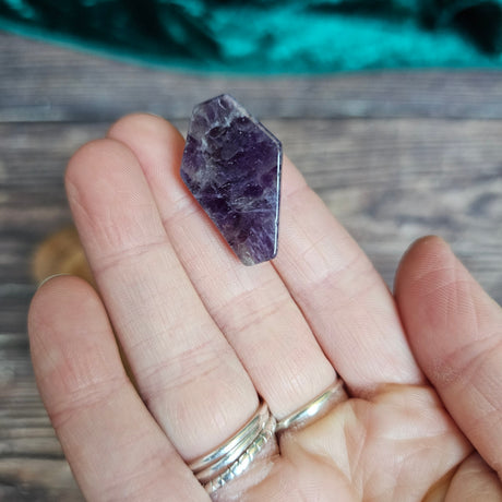 An Amethyst crystal shaped as a coffin is being held in someone's hand