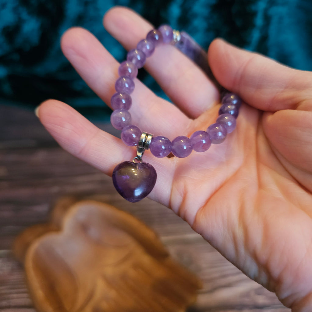 A hand holding a purple amethyst bead bracelet with a heart-shaped bead and bar quartz accents.