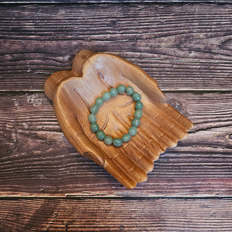A tumbled crystal bracelet in shades of green, placed on a wooden bracelet holder shaped like a pair of hands.