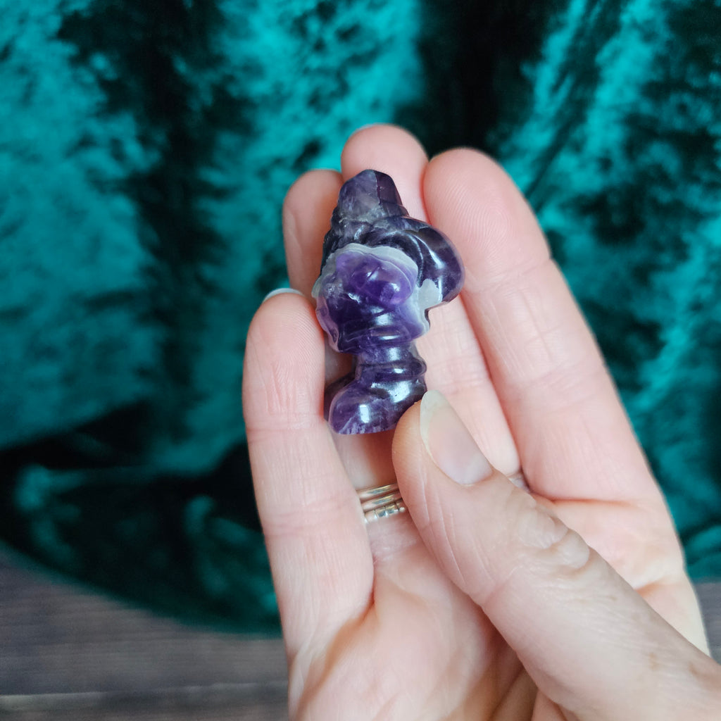 A carved Amethyst crystal Santa figure held in a person's hand.