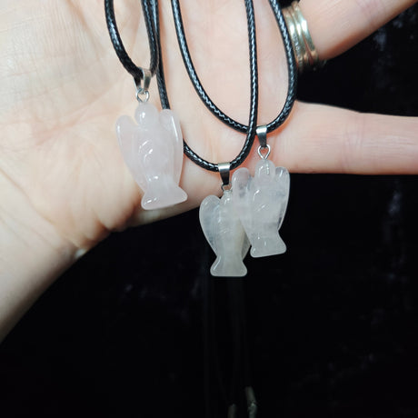 Three angel-shaped crystal pendants attached to black cord necklaces, held in a person's hand.