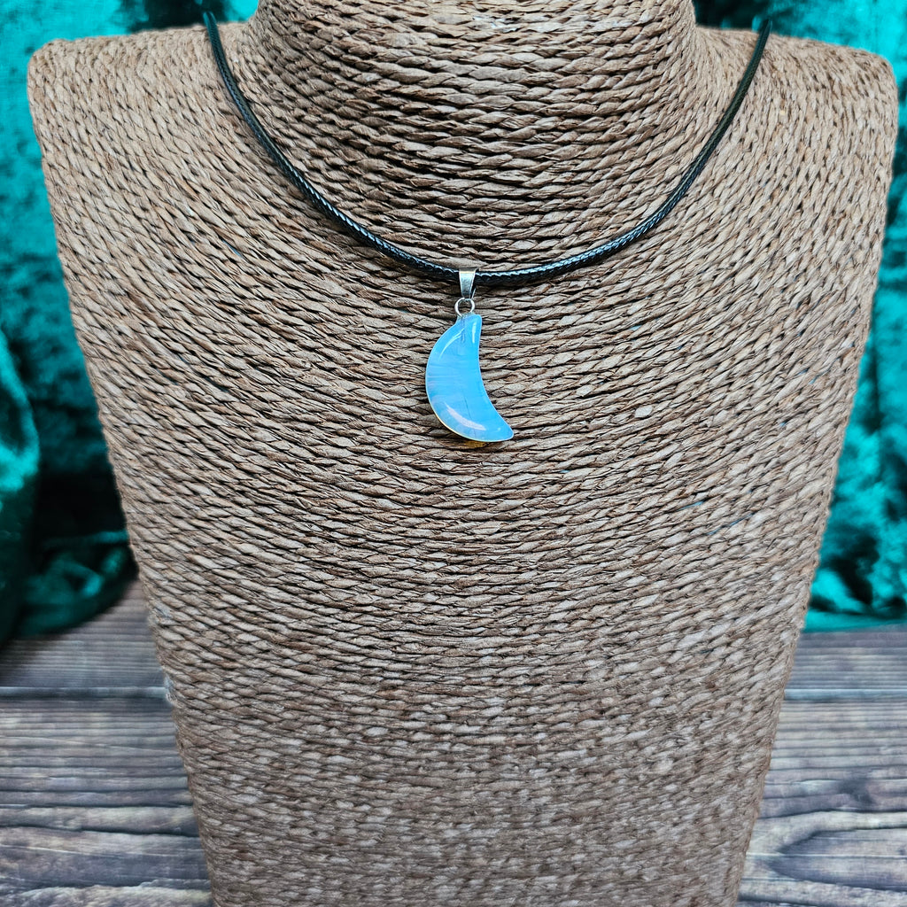 A crescent moon shaped crystal pendant on a black cord displayed on a mannequin 