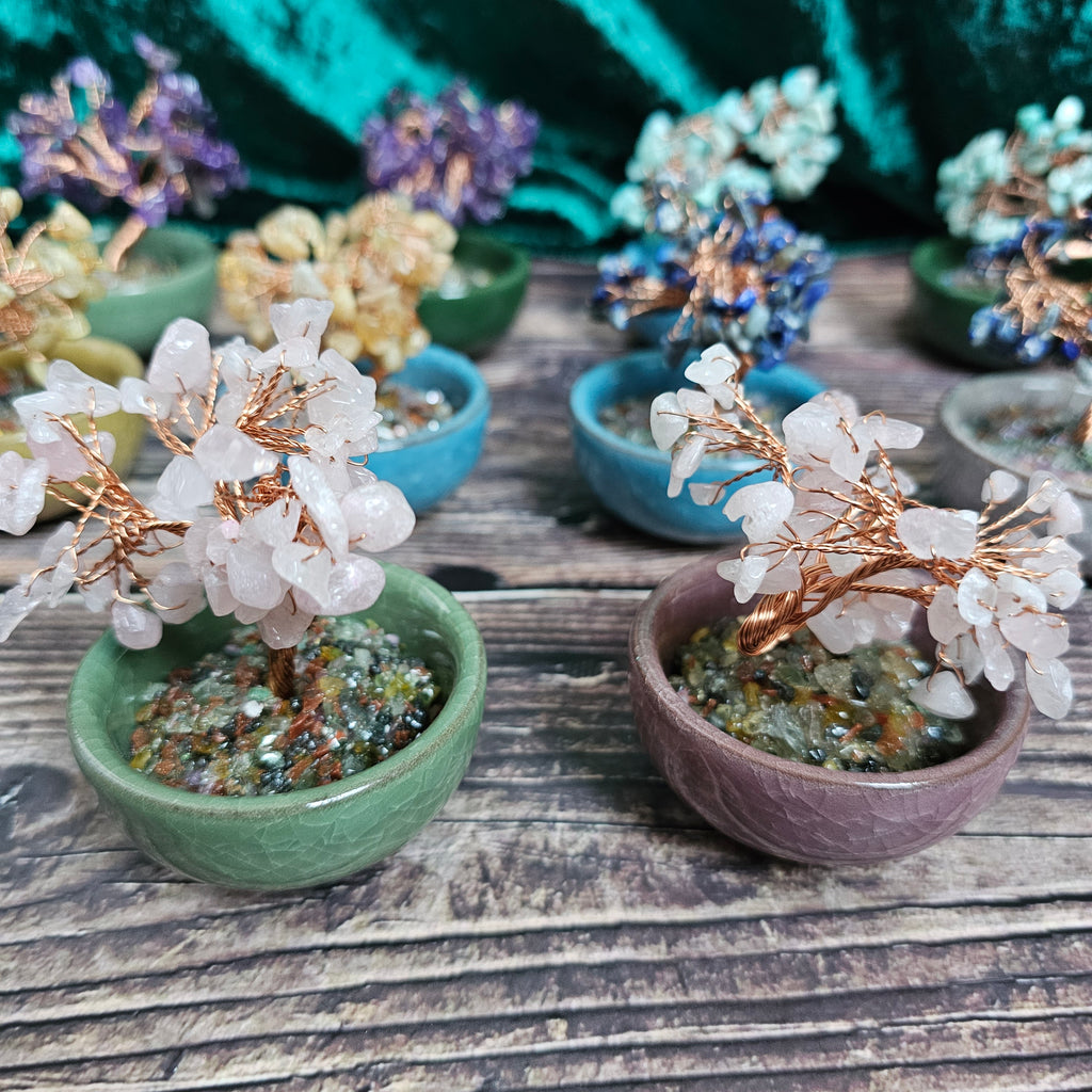 A collection of ceramic tea bowls with a crystal tree decoration on a wooden surface, with colours including green, blue, and purple.