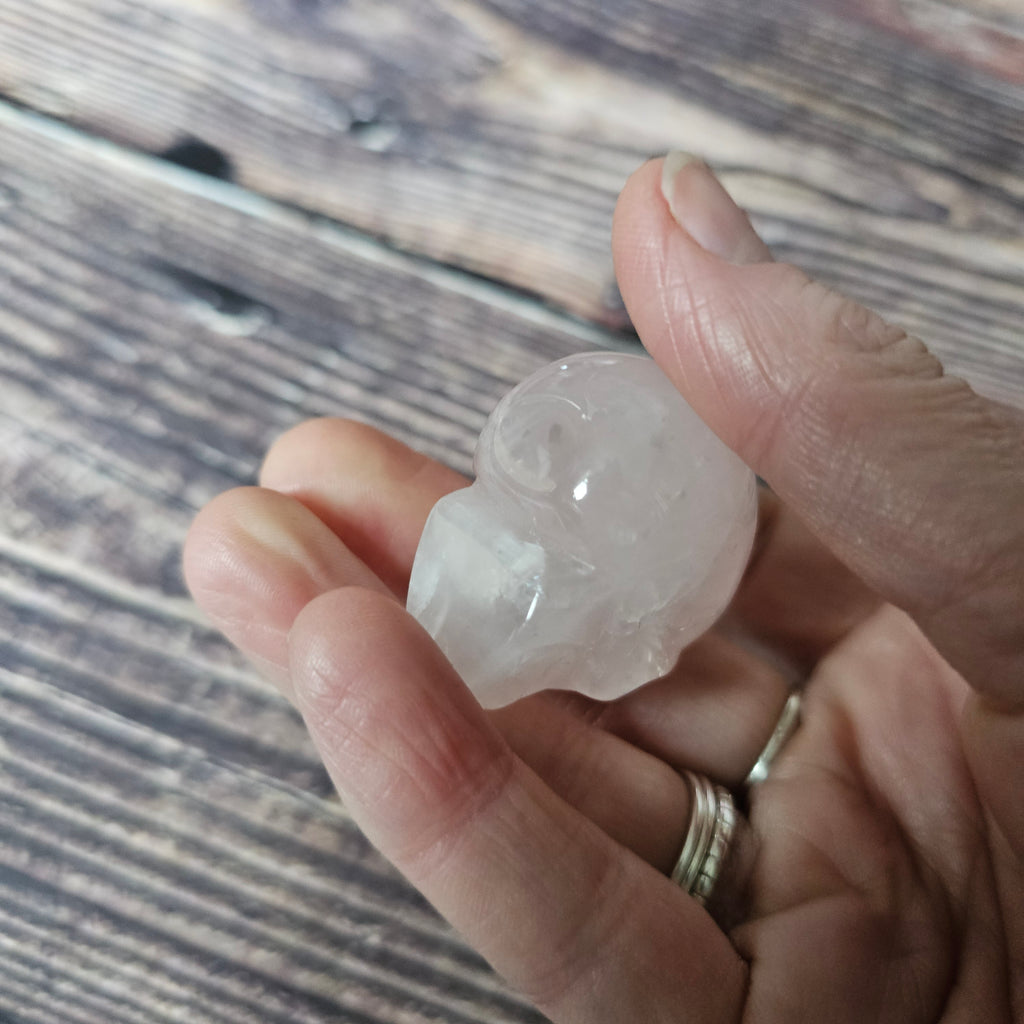 A carved pink crystal skull held in a hand