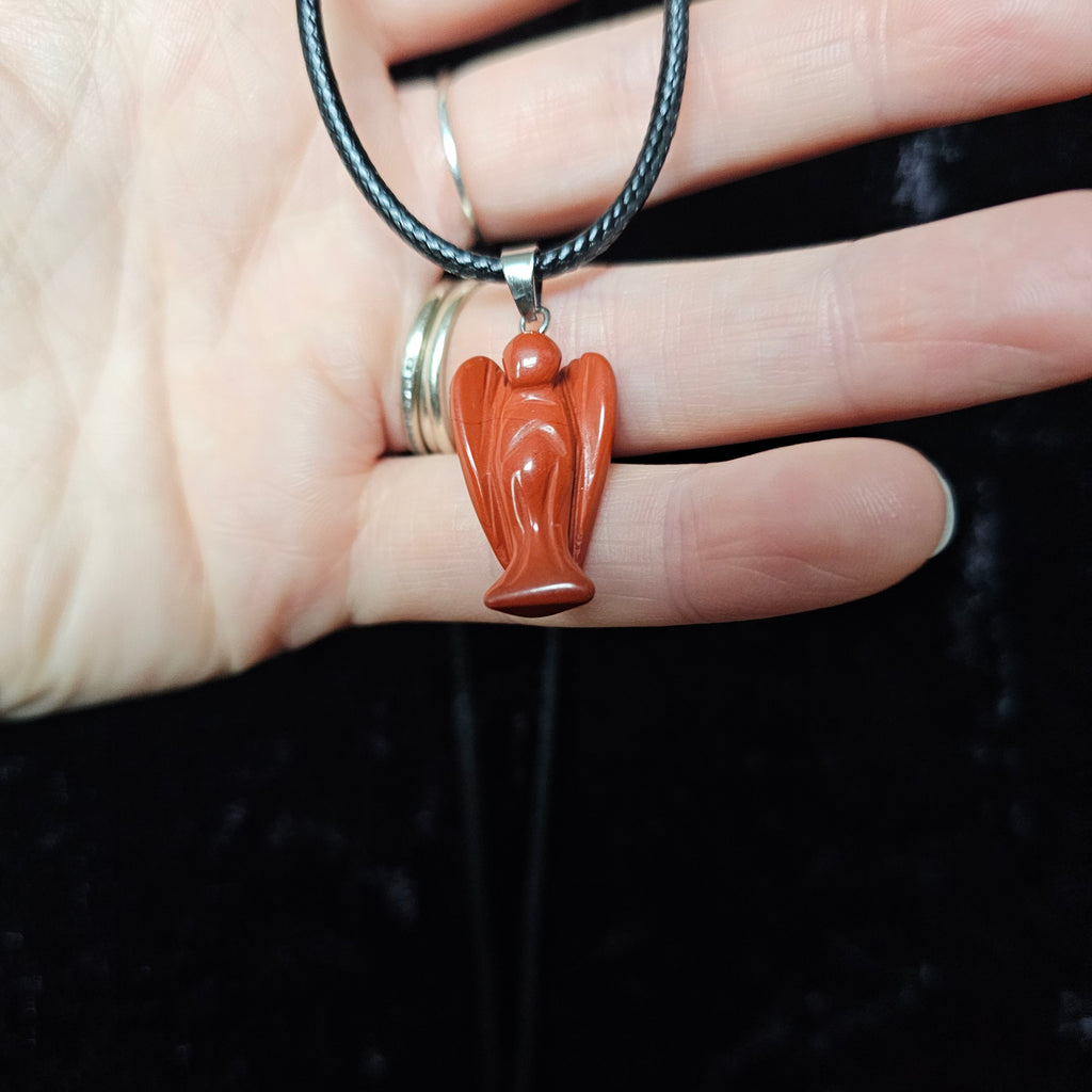 An angel-shaped crystal pendant attached to black cord necklace held in a person's hand on a dark background