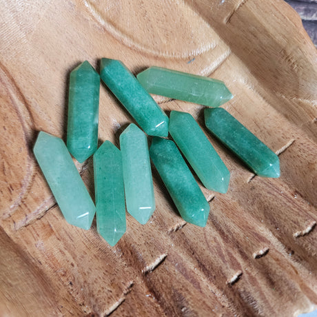 Small green double pointed crystals held in wooden carved hands