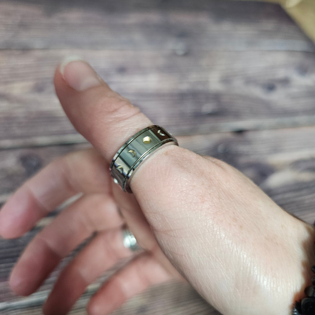 Someone wearing a polished silver ring with moon phase cut-outs and gold details.