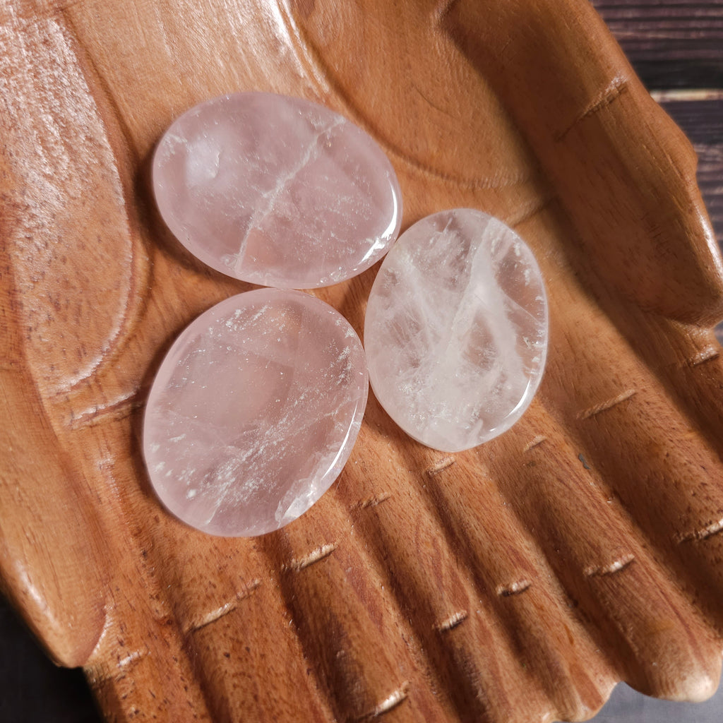 Three pink polished crystal thumbstones resting on a wooden surface
