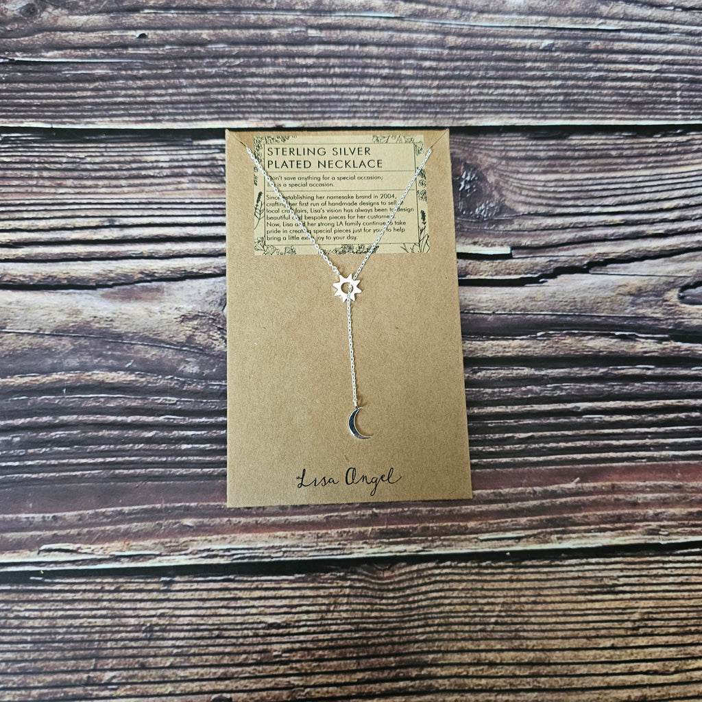 A silver lariat necklace featuring a crescent moon and an open sun charm laid on a wooden background. 