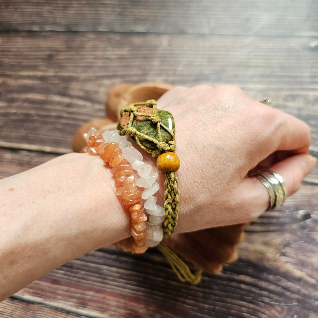 A sand-coloured crystal cord bracelet with an example crystal inside, on a wrist alongside other crystal chip bracelets 