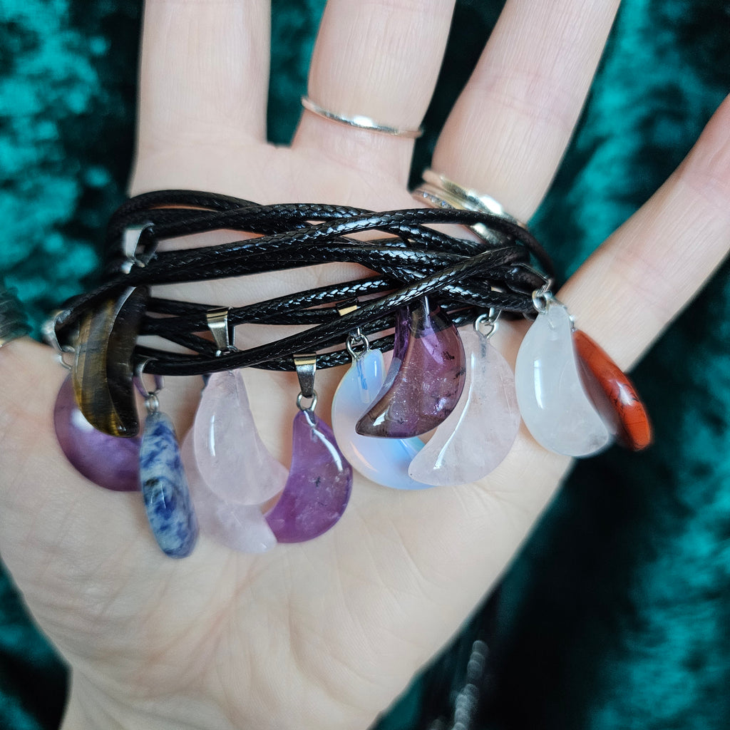 A collection of crescent moon shaped crystal pendants in various colours, held in someone's hand