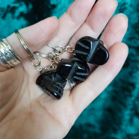 Three Black Obsidian carved crystal skull key chains in someone's hand