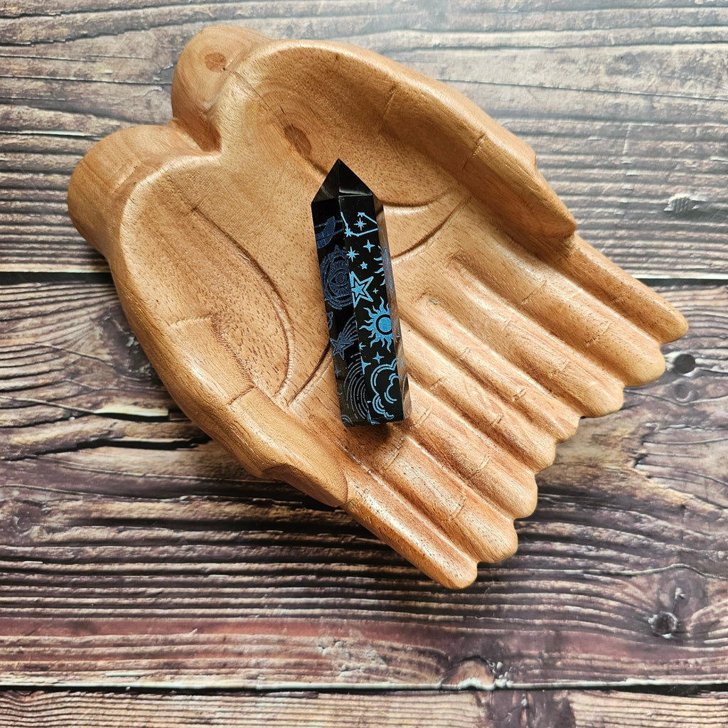 A Black Obsidian Generator with celestial designs displayed on a wooden hand-shaped tray.