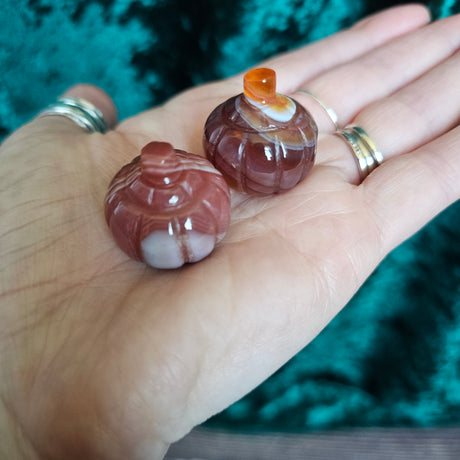 Two carved Carnelian crystal pumpkins being held in someone's hand
