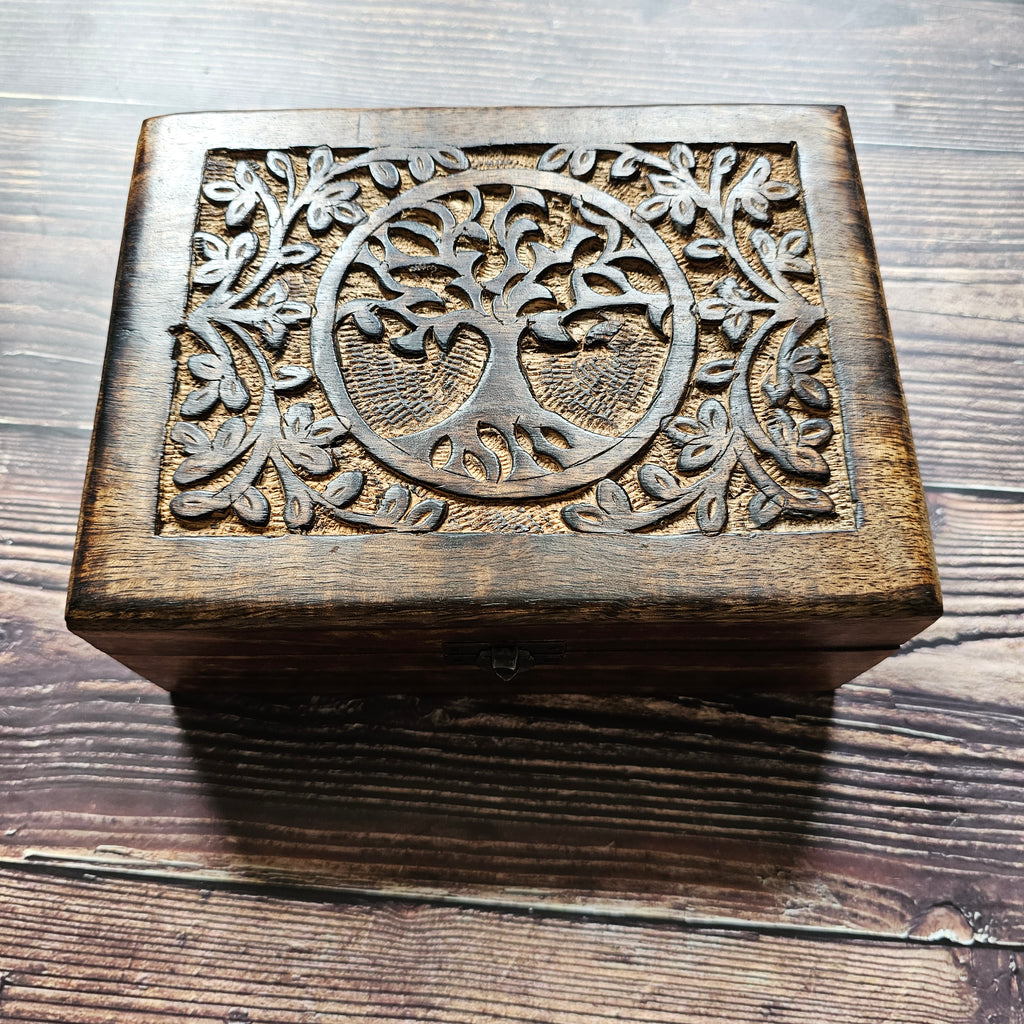 A wooden box with a carved Tree of Life design on the lid, placed on a wooden surface.