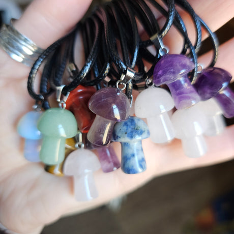 A collection of mushroom-shaped crystal pendants in various colours attached to black cords, held in a person's hand.