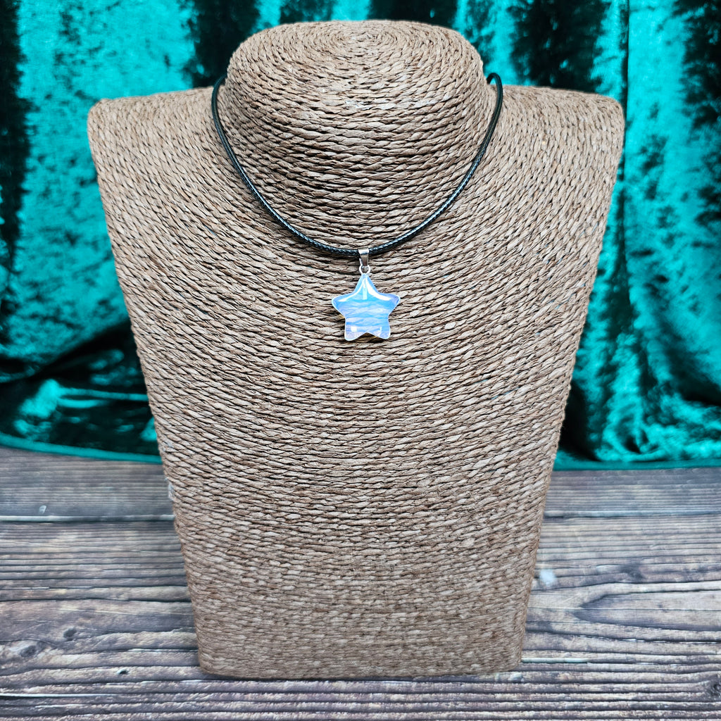 A star-shaped crystal pendant displayed on a brown mannequin, with a black cord.