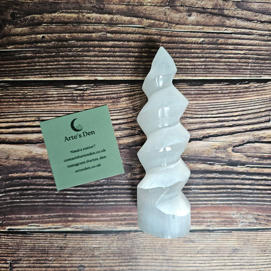 A selenite "unicorn horn" which is a spiral tower, laid on a wooden background