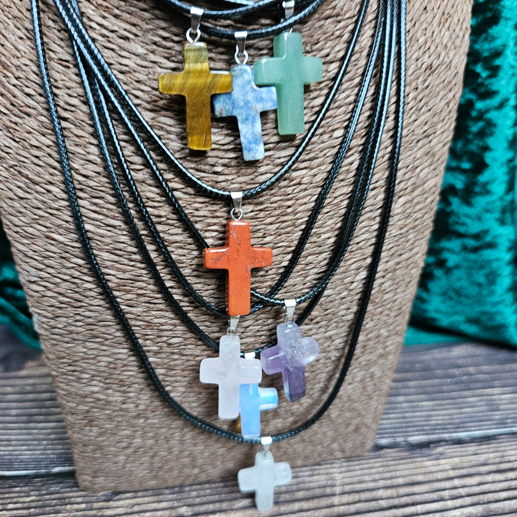 Several cross-shaped crystal pendants with a black cord necklace displayed on a mannequin.