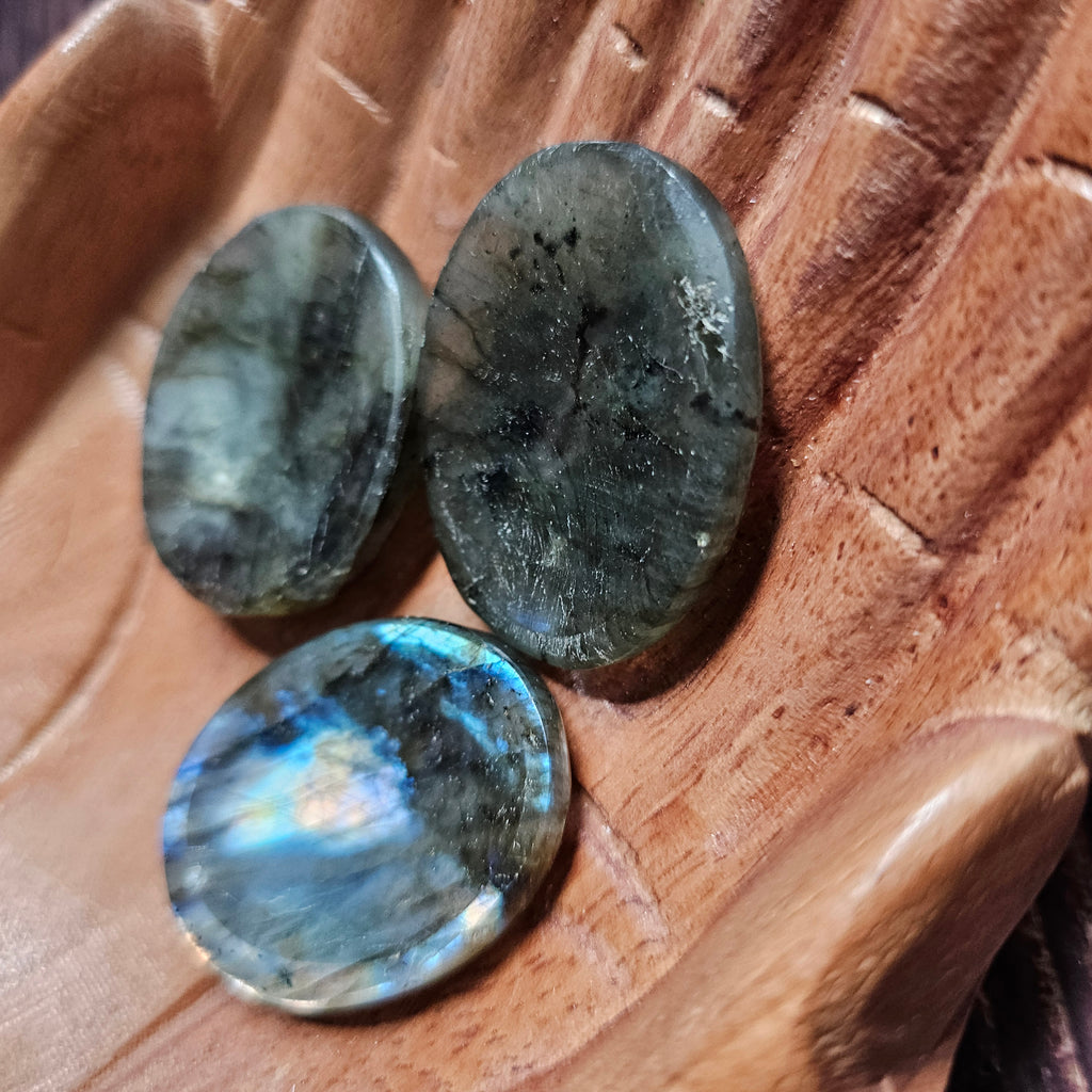 Three grey polished crystal thumbstones resting on a wooden surface