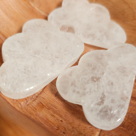 Carved clear quartz crystals shaped like clouds, placed on a wooden surface.