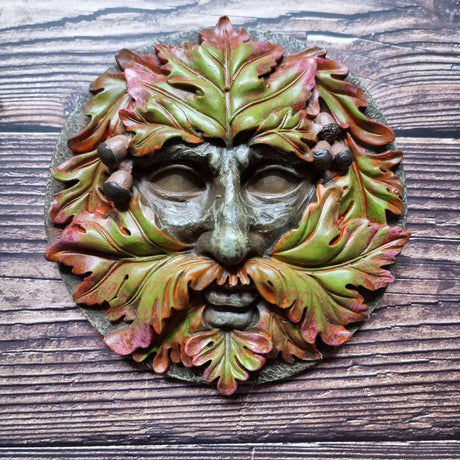 A round plaque in a green man design against a wooden background