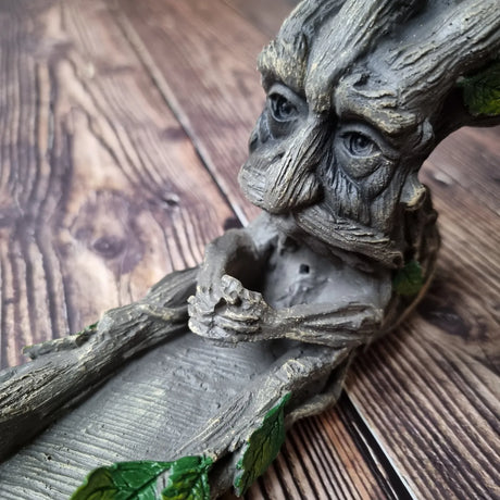 A resin incense holder in the shape of a stylised Green Man character, with leaf patterns for eyes and branches for a mouth and nose.