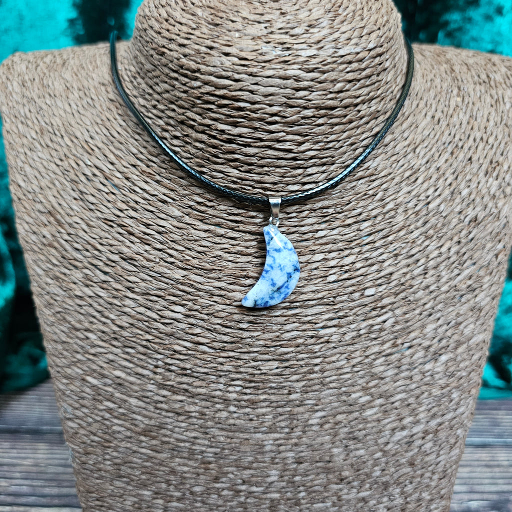 A crescent moon shaped crystal pendant on a black cord displayed on a mannequin 