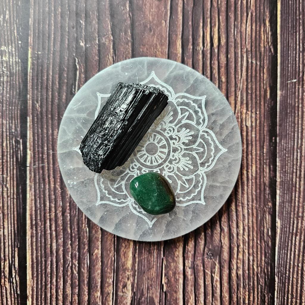 A round selenite charging plate with a mandala pattern etched into it, placed on a wooden surface, with two crystals placed on top