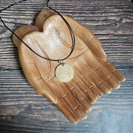 A coin-shaped crystal citrine pendant, attached to a black cord, displayed on a wooden pair of hands