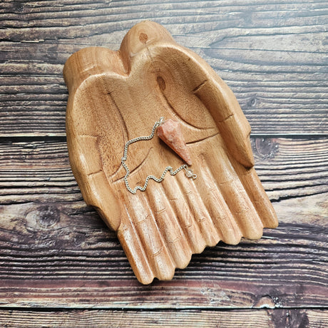 A sunstone pendulum, displayed on a wooden surface.