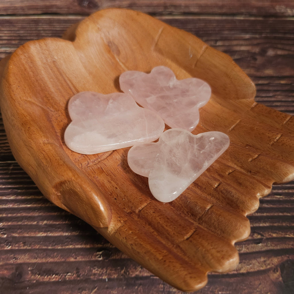 Carved rose quartz crystals shaped like clouds, placed on a wooden surface.